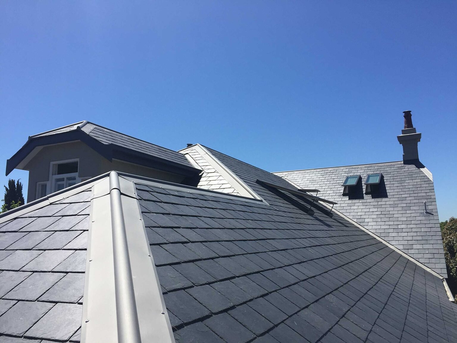 Slate roofs, dormers and lead detailing beneath a blue sky